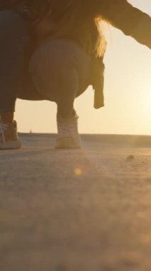 Dikey video. Günbatımında Sıcak Güneş Işığı ve Arkaplanda Gölgeler ile Beton Yüzeyde Siyah ve Beyaz Kedi Sevmek İçin Çömelen Kadın