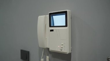 Duvara monte edilmiş, küçük mavi ekranlı, sarmalanmış kablo, ve gri bir duvardaki düğmeler