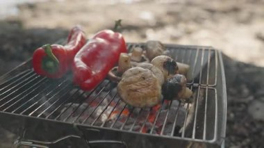 Kırmızı çan biberleri ve mantarlar kızgın kömürün üstünde pişiyor, bir el de sebzeleri doğaya yakın bir yerde ayarlıyor.