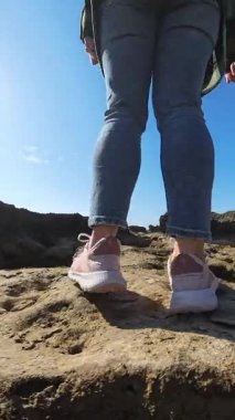 Kayalık bir deniz kıyısında, parlak güneşli bir gökyüzünün altında, arka planda okyanus görünen bir kadının ilk insan görüntüsü.