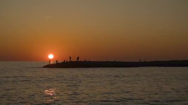 Balıkçıların Balık Çubuklarıyla Rocky Rıhtımında Zaman Hızı Denizin Üzerindeki Günbatımını Silüet 'te Portakal Gökyüzü ile izliyor