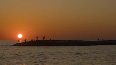 Balıkçıların Zaman Hızına Yaklaş Balıkçı Çubuklarıyla Bir Rocky Rıhtımında Duruyorlar Gün batımında Denizin üzerinde Siluette bir Orange Sky ile