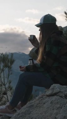 Dikey video. Bir fincan sıcak çay ve Karlı Dağ Tepeleri 'nin nefes kesici manzarası ve Bulutlu Günbatımı Gökyüzü, Kupadan Buhar Yükseliyor,