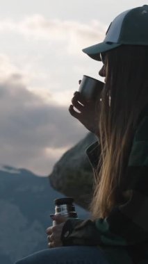 Bir uçurumun kenarında oturmuş sıcak çay içerken Sunset 'te Karlı Dağ Dağları' na bakan, Kupadan Buhar Yükseliyor, Yalnızlığı ve Yansımayı temsil eden