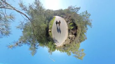 Virajlı bir yolda yürürken el ele tutuşan iki gezgin, Küçük Gezegen Perspektifinde yakalanarak, Yolculuklarının ve Bağlantılarının benzersiz bir görüntüsünü oluşturuyorlar.