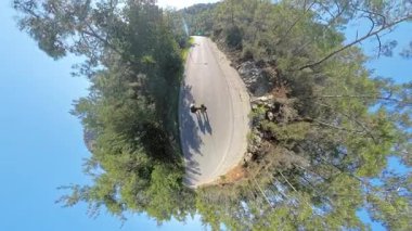 Ağaçlarla çevrili bir dağ yolunda el ele yürüyen bir çift, Küçük Gezegen Efekti, Macera ve Doğa Keşfi 'ni temsil ediyor.