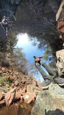 Dikey video. 360 Derece Arkaplanda Mavi Gökyüzü ve Ağaçlı Küçük Bir Derenin Üzerinde Yürüyen Kayalıklara Yürüyen Bir Yürüyüşçü Perspektifi