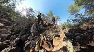 Ağaçlarla çevrili bir dağ deresi içinde Rocky Arazisi 'ne tırmanan iki yürüyüşçünün geniş açılı görüntüsü