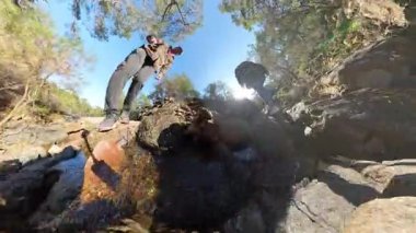 Temiz Su ve Güneş Işığı Yansımaları ile Rocky Nehri 'nden Geçen İki Gezgin Düşük Açı Görünümü