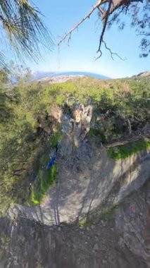 Dikey video. Sırt çantalı bir adam Forested Hills 'in Manzarası' nı, bir sahil kasabasını ve bir uçurumdan uzak dağları hayranlıkla seyrediyor.