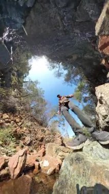 Dikey video. 360 Derece Arkaplanda Mavi Gökyüzü ve Ağaçlı Küçük Bir Derenin Üzerinde Yürüyen Kayalıklara Yürüyen Bir Yürüyüşçü Perspektifi