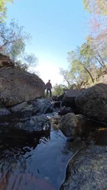 Dikey video. Özenle Yürüyen Adam Arkaplanda Güneş Işığı ve Ormanla Küçük Dağ Kayalıklarında Yürüyor