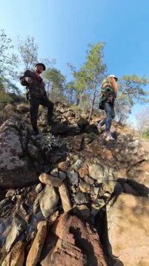 Dikey video. Ağaçlarla çevrili bir dağ deresi içinde Rocky Arazisi 'ne tırmanan iki yürüyüşçünün geniş açılı görüntüsü