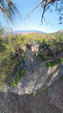Dikey video. Sırt çantalı bir adam Forested Hills 'in Manzarası' nı, bir sahil kasabasını ve bir uçurumdan uzak dağları hayranlıkla seyrediyor.