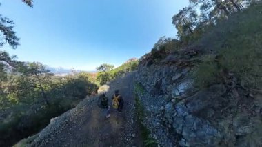 İki Gezgin Dik Dağ Yolu 'nda, Orman Tepeleri' nin Panoramik Manzarası ve Uzak Kıyı Kasabası 'yla yürüyor.