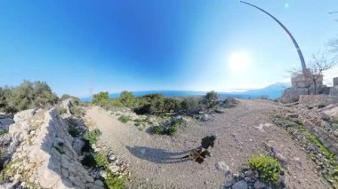 Dağın zirvesine ulaşan iki yürüyüşçü, aşağıdaki deniz ve vadiyi göz kamaştırıcı bir şekilde görüyor ve açık mavi gökyüzü altında güneş ışığıyla 360 derecelik bir perspektifle yakaladılar.
