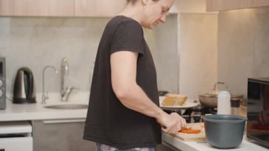 Modern Kitchen 'da Ahşap Kesme Tahtasında Kırmızı Biber Kesen Siyah Tişörtlü Kadın ve Soba ve Mikrodalga Yakınında