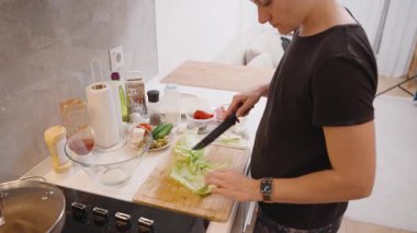 Salatalık, domates ve baharat gibi malzemelerle çevrili, Parlak Modern Mutfakta Marul Kesen Kadın Görünümü, Taze Salata Hazırlama