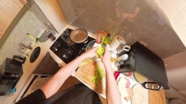 Küçük bir Mutfakta, Yeni Malzemeler ve Pişirme Aletleri ile çevrili bir kaseye doğranmış Marul Ekleyen Bir Kişinin 360 derece Genel Görünümü