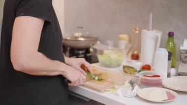 Marul, Domates ve Baharat Gibi Taze İçindekiler ile çevrili Modern Mutfak 'ta Tahta Kesme Tahtasında Salatalık Kesen Bir Kişi Görünümü