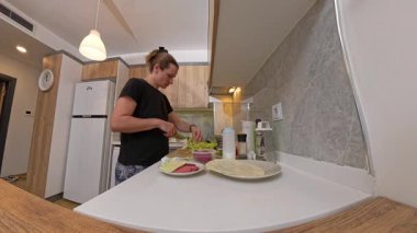 Modern bir Mutfakta Yemek Hazırlayan Bir Kadının Geniş Açı Görünümü, Peynir, Sosis ve Tortilla Paketleriyle Bir Tezgahta Sebze Kesme