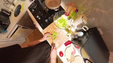 Tahta kesim tahtasındaki salatalık kesme tahtasının 360 derecelik birinci şahıs görüntüsü. Küçük bir mutfakta yeni malzemeler ve pişirme aletleriyle çevrili.