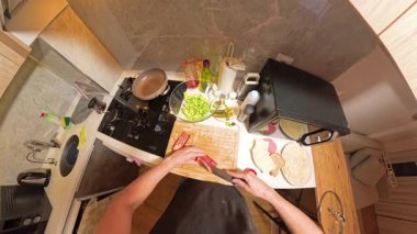 Küçük bir mutfaktaki ahşap kesim tahtasında kırmızı çan biberi kesen birinin 360 derecelik birinci derece görüntüsü Taze Malzemeler ve Yemek Utensilleri ile çevrili.