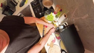 Tahta kesim tahtasında kırmızı çan biberi kesen bir kişinin 360 derece yukarıdan görünüşü, Küçük bir mutfakta taze malzemeler ve mutfak gereçleri ile çevrili.