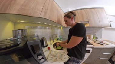 Taze sebzeler, yemek takımları, modern ahşap dolaplar ve aperatiflerle çevrili mutfak lavabosunda yıkanmış bir kadının geniş açılı görüntüsü.