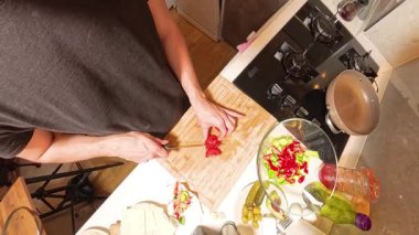 Tahta kesim tahtasında domates kesen bir insanın 360 derecelik birinci derece görüntüsü, yanında da cam bir kase taze salata ve pişirme malzemeleri var.