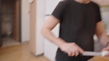 Tezgahtaki cam kasede zeytin, domates ve biber içeren taze salata ile ahşap kesim tahtasında Brynza peynirini doğrayan ellerin yakın çekimi