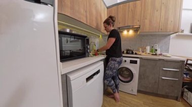 Çıplak Ayaklı Kadın Ahşap Dolaplı Mutfak 'ta Sebze Hazırlıyor, Lavabonun Yanında Duran, Buzdolabı, ve Bulaşıkçı, Yıkama ve Organize Etme Taze İçindekiler