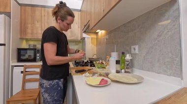 Modern Kitchen 'da Kara Gömlekli Kadın Ahşap Dolaplı ve Beyaz Tezgahlı Salata Hazırlıyor Cam Kasede İçindekileri Karıştırıyor, Geniş Açı Görüş