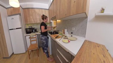 Çağdaş Mutfakta Ahşap Dolaplar ve Beyaz Tezgahlı Kadın Ocakta Çıplak Ayakla Yemek Pişiriyor. Ev Yemekleri Konsepti