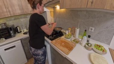 Kara Gömlekli Kadın Küçük Mutfağa Bakarken Fırında Yumurta ve Sosis Pişiriyor. Kahvaltı Hazırlama Konsepti