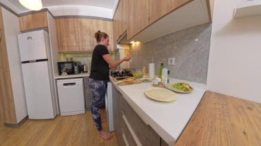 Modern Kitchen 'da Kara Gömlekli Kadın Tezgahta Ahşap Dolaplar ve Çeşitli Malzemeler ile Gaz Fırınında Pişiyor. Ev Yemekleri Konsepti