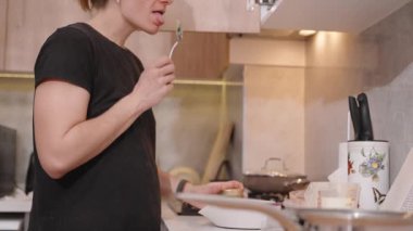 Modern mutfakta ahşap dolaplarla yemek pişirirken Kara Gömlekli Kadın Spoon 'dan yemek tadıyor. Gıda Hazırlama Konsepti