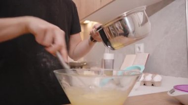 Paslanmaz çelikten yapılmış sütü Sarı Vuruşlu Cam Kase 'ye döken, Karıştırmak için Bir Fırça, Ilık Işıklı Mutfak Arkaplanı kullanan Kadın' ın Yakın Çekimi