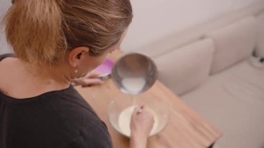 Ahşap Mutfak Tezgahında çırpınırken Sarı Vuruşlu Cam bir kaseye Paslanmaz Çelik Tencereden Ilık Süt Döken Kadın Görünümü