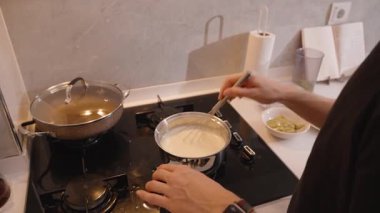 Mutfak tezgahında malzemelerle birlikte paslanmaz çelik tencerenin içinde kremalı beyaz karışımı çırpma manzarası.