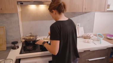 Çağdaş Mutfakta Bir Tencere, İçindekiler ve Tezgahta Pişirme Aletleri Karıştıran Bir Ocakta Duran Kadın