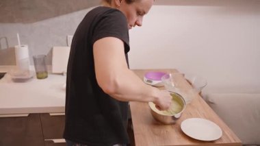 Ahşap mutfak tezgahı, yemek tarifi kitabı ve içindekiler yakınındaki bir tabakta kalın yeşil bir karışım hazırlarken elinde çırpı tutan kadın.