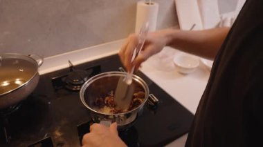 Mutfak tezgahı Mutfak Aletleri ve Malzemeleri Yakınındaki Silikon Spatula Kullanarak, Bir Tenceredeki Kurutulmuş Meyveleri Gaz Fırınında Karıştırır