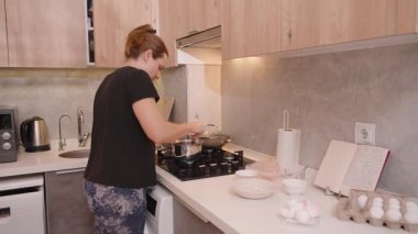 Geniş Açı Kadın Atışı Modern Mutfakta Gaz Fırınında Pişirme, Kurumuş Meyveler, Tarif Defteri ve Tezgahın İçindekiler ile Bir Tencereyi Karıştırma