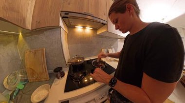 Modern bir mutfağın gaz ocağında, tencerede kurutulmuş meyveler pişiren kadın. Geniş açılı çarpık perspektif.