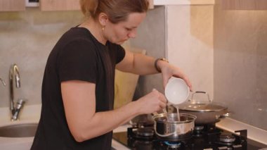 Karışımı karıştırırken, Beyaz Kâse 'den ocağın üzerindeki bir tencereye Sıvı döken Kadının Yakın Çekimi