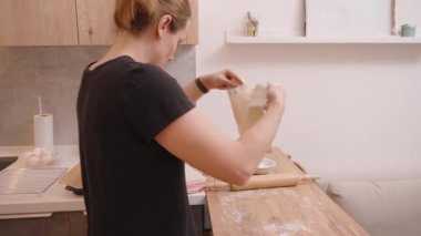 Kadın, Parşömen kağıdıyla bir tepsiye yuvarlanmış hamur işi yerleştiriyor. İçi fırın malzemeleri ve yemek tarifi kitabıyla çevrili.