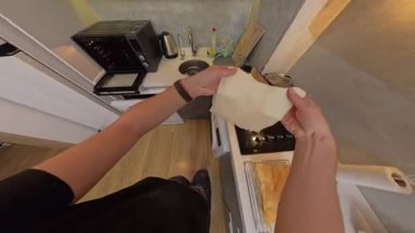 Modern bir mutfakta, fırının yanında pişmemiş hamur işiyle bir tepsiyi elinde tutan kadının genel görünümü.