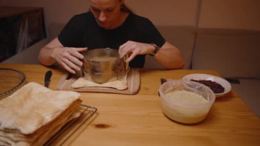 Bir kadın ahşap kesim tahtasındaki Yuvarlak Kek Yüzüğünü kullanarak Pasta Katmanlarını Dikkatle Kesiyor