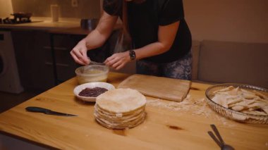 Ahşap bir masa üzerinde hamur işi tabağıyla bir kase meyveli reçelin paketini açan kadın.